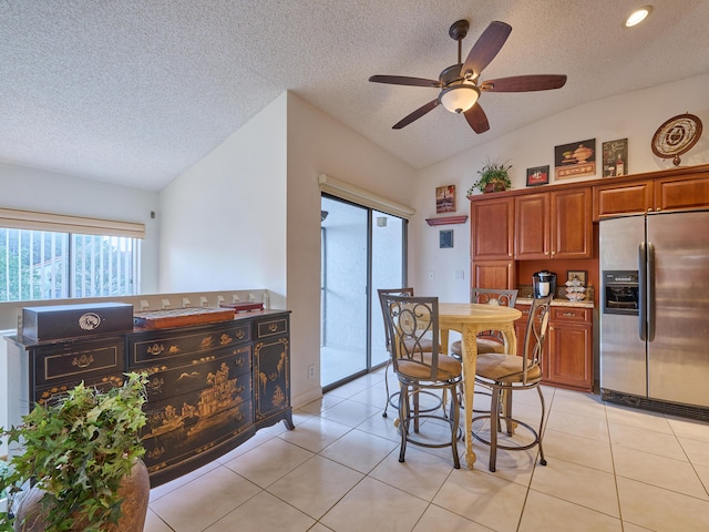 kitchen with brown cabinets, light tile patterned floors, light countertops, vaulted ceiling, and stainless steel fridge with ice dispenser