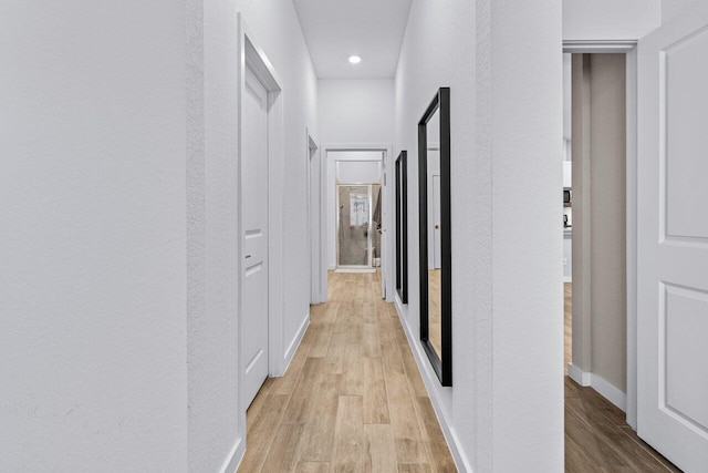 hall featuring light wood-type flooring, baseboards, and a textured wall