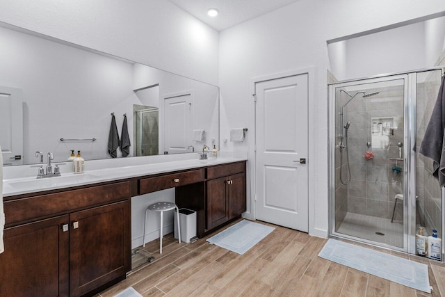 bathroom with a stall shower, double vanity, a sink, and wood finished floors