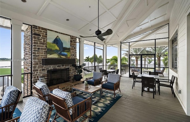 sunroom / solarium with ceiling fan, a stone fireplace, beam ceiling, and a wealth of natural light