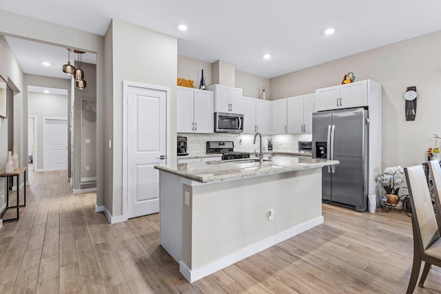 kitchen with a sink, appliances with stainless steel finishes, light stone countertops, light wood finished floors, and an island with sink