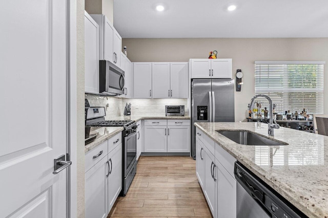 kitchen with white cabinets, light wood-style flooring, appliances with stainless steel finishes, a sink, and backsplash