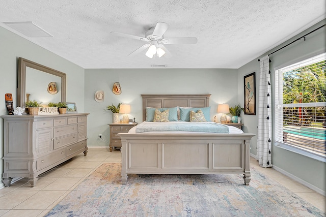 bedroom featuring light tile patterned floors, visible vents, a ceiling fan, a textured ceiling, and baseboards