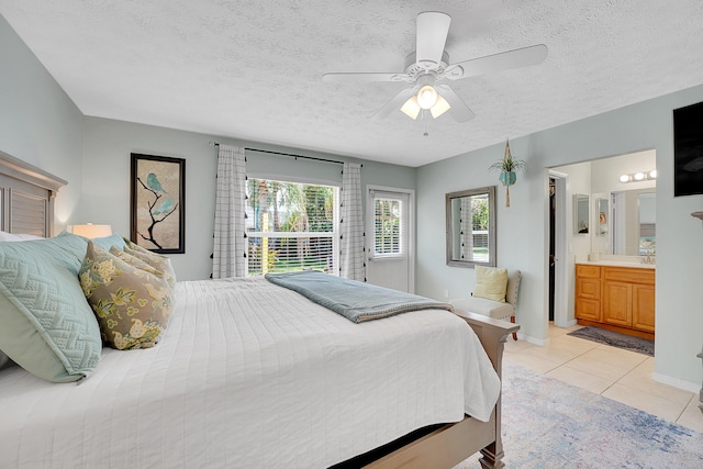 bedroom with baseboards, ceiling fan, ensuite bathroom, a textured ceiling, and light tile patterned flooring