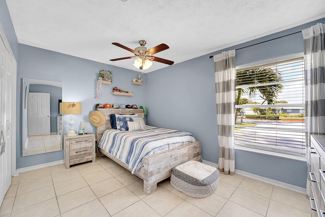 bedroom featuring light tile patterned floors, ceiling fan, baseboards, and a textured ceiling