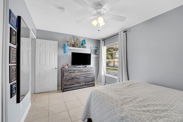 bedroom featuring ceiling fan, a textured ceiling, baseboards, and light tile patterned floors