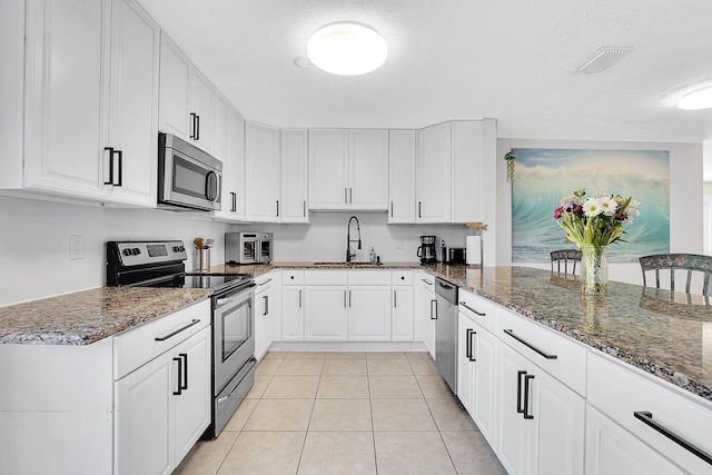 kitchen featuring stainless steel appliances, white cabinetry, a sink, and dark stone countertops