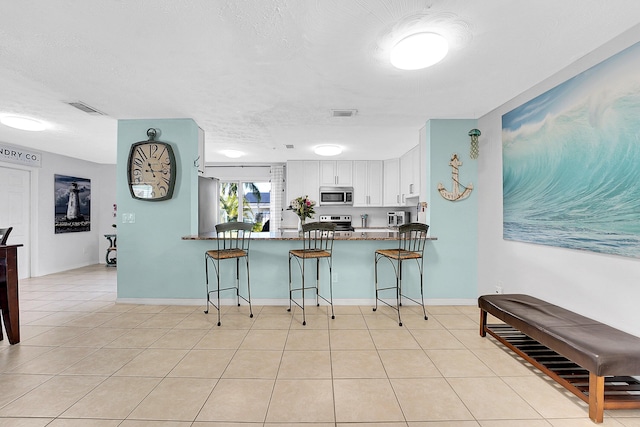 kitchen featuring light tile patterned floors, stainless steel appliances, white cabinets, a peninsula, and a kitchen bar