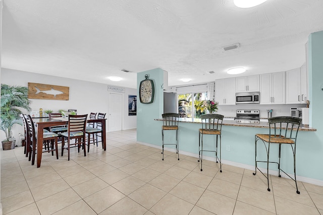 kitchen featuring a peninsula, a breakfast bar, visible vents, white cabinets, and appliances with stainless steel finishes