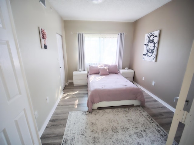 bedroom with a textured ceiling, wood finished floors, visible vents, and baseboards