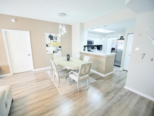 dining space with a textured ceiling, light wood finished floors, and baseboards