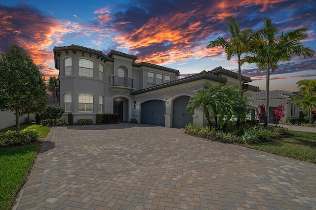 mediterranean / spanish-style house with decorative driveway, a tile roof, stucco siding, an attached garage, and a balcony