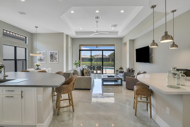 kitchen with a breakfast bar area, visible vents, white cabinets, open floor plan, and a tray ceiling