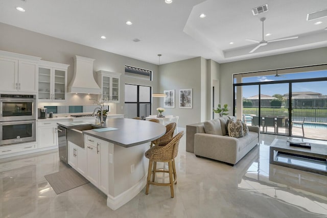 kitchen featuring a center island with sink, custom range hood, visible vents, appliances with stainless steel finishes, and white cabinets