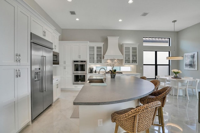 kitchen with marble finish floor, visible vents, a sink, built in appliances, and premium range hood