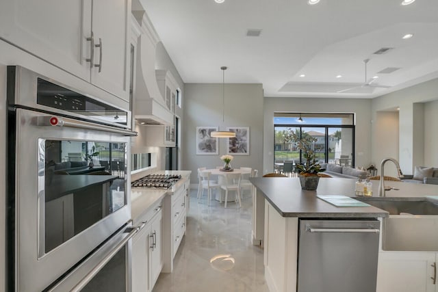 kitchen with a sink, white cabinets, appliances with stainless steel finishes, a tray ceiling, and pendant lighting