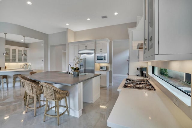 kitchen with a kitchen breakfast bar, white cabinetry, an island with sink, and built in appliances