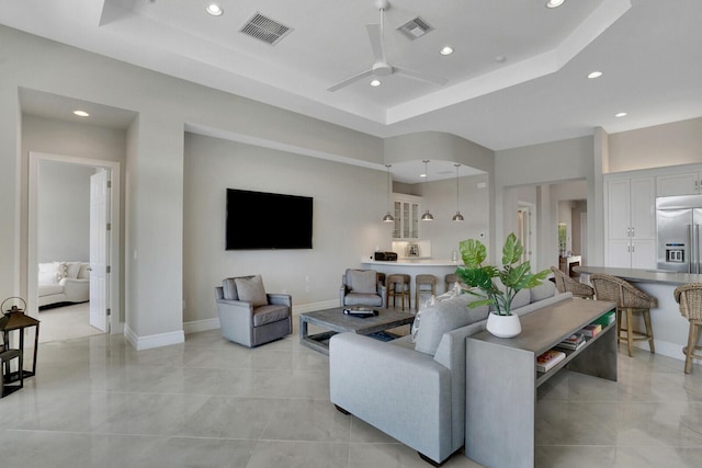 living room with a tray ceiling, visible vents, and a ceiling fan