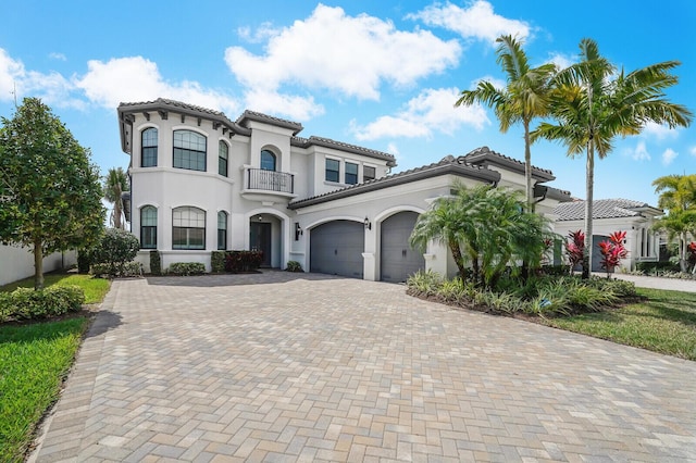 mediterranean / spanish-style home featuring a garage, a balcony, a tiled roof, decorative driveway, and stucco siding