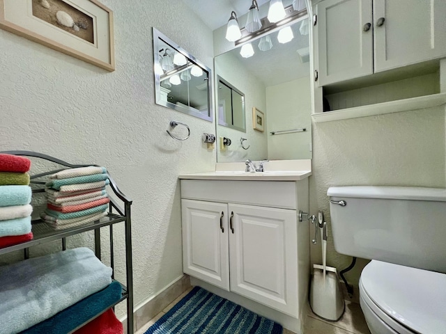 half bath featuring vanity, toilet, a textured wall, and baseboards