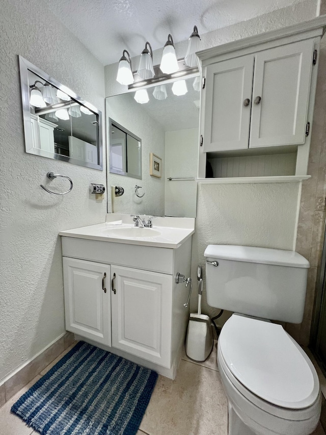 bathroom featuring baseboards, toilet, vanity, and a textured wall