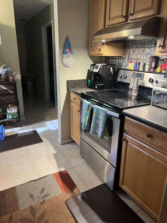 kitchen featuring under cabinet range hood, dark countertops, stainless steel electric range oven, and light tile patterned flooring