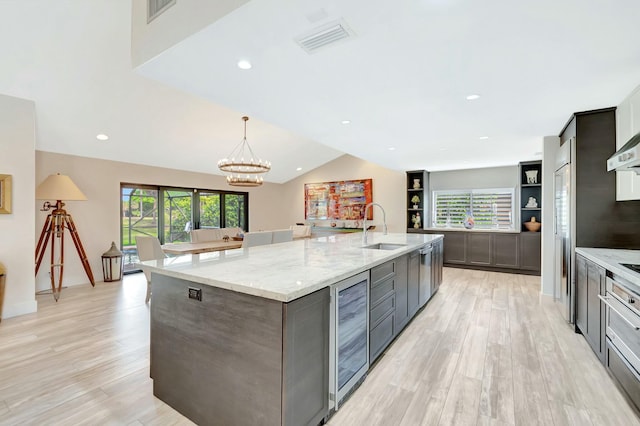 kitchen with wine cooler, a sink, visible vents, light stone countertops, and a large island with sink