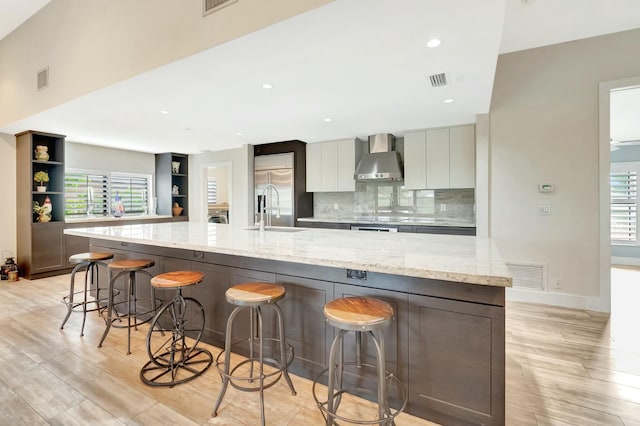 kitchen with visible vents, a kitchen breakfast bar, light stone countertops, wall chimney exhaust hood, and modern cabinets