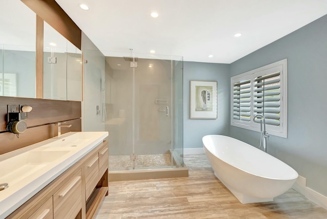 full bathroom featuring double vanity, a stall shower, a soaking tub, and wood finished floors