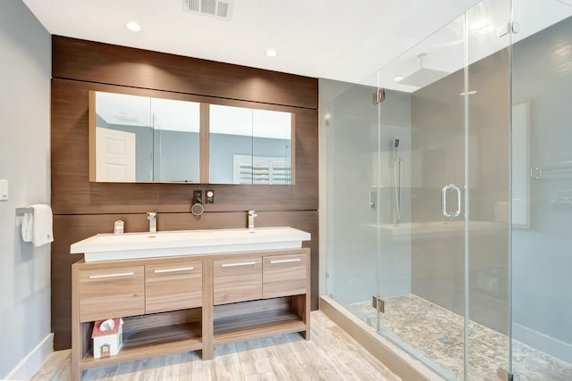 full bath featuring double vanity, a stall shower, visible vents, and wood finished floors