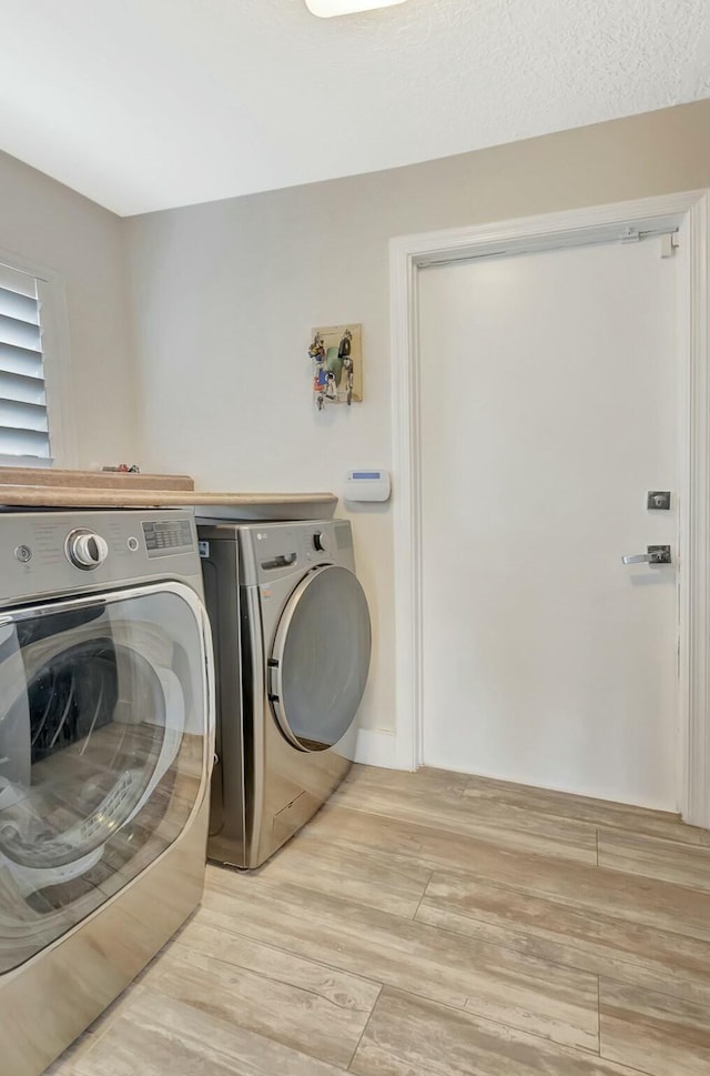 clothes washing area with laundry area, light wood-style flooring, and washer and clothes dryer