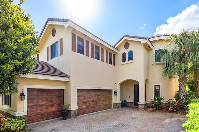 mediterranean / spanish-style home with a garage, decorative driveway, a tiled roof, and stucco siding