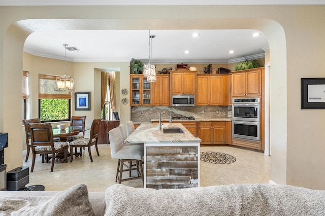 kitchen with arched walkways, tasteful backsplash, appliances with stainless steel finishes, brown cabinetry, and a sink