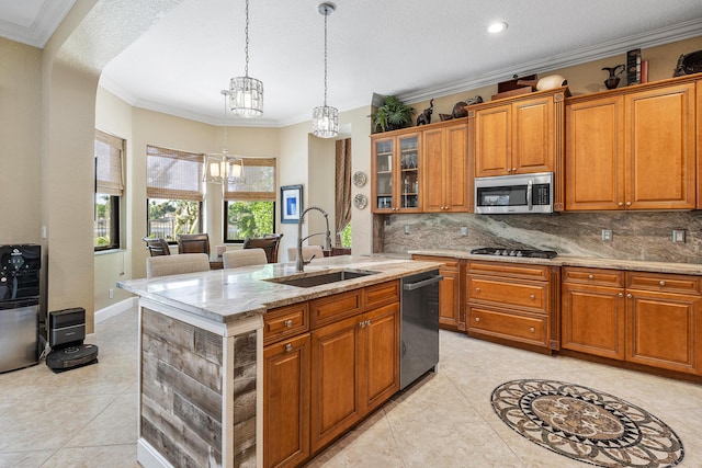 kitchen featuring stainless steel microwave, brown cabinetry, a sink, an island with sink, and dishwasher