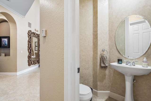 bathroom featuring baseboards, visible vents, a textured wall, toilet, and ornamental molding