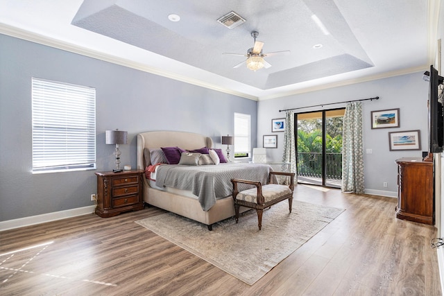 bedroom with light wood-type flooring, a tray ceiling, access to outside, and visible vents