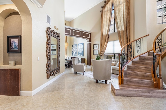 interior space with visible vents, baseboards, a towering ceiling, stairway, and crown molding