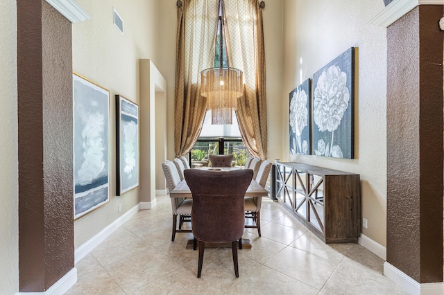 dining area featuring baseboards, visible vents, a textured wall, a towering ceiling, and tile patterned floors