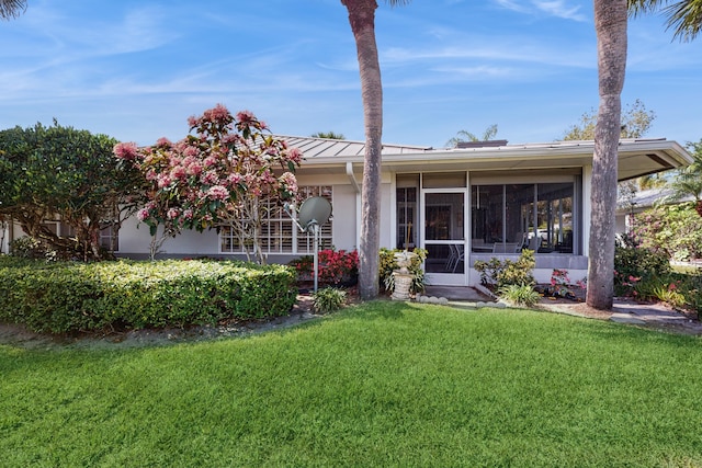 view of front facade with stucco siding, a front yard, a sunroom, a standing seam roof, and metal roof