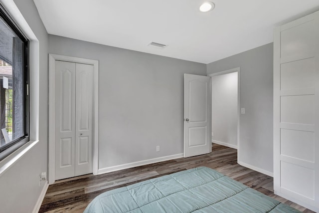 unfurnished bedroom with a closet, wood finished floors, visible vents, and baseboards