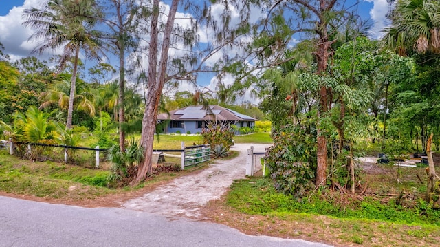 exterior space with a fenced front yard, solar panels, dirt driveway, a gate, and a front lawn