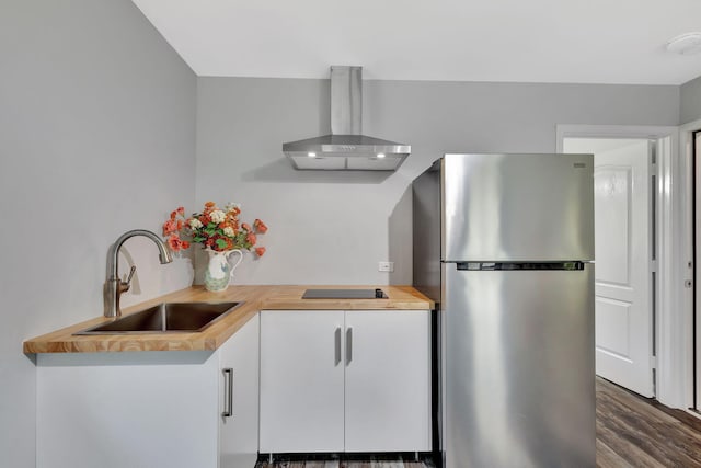 kitchen with wooden counters, freestanding refrigerator, white cabinets, a sink, and wall chimney range hood