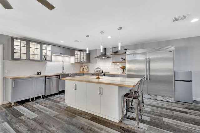 kitchen with stainless steel appliances, tasteful backsplash, visible vents, wall chimney range hood, and wood counters