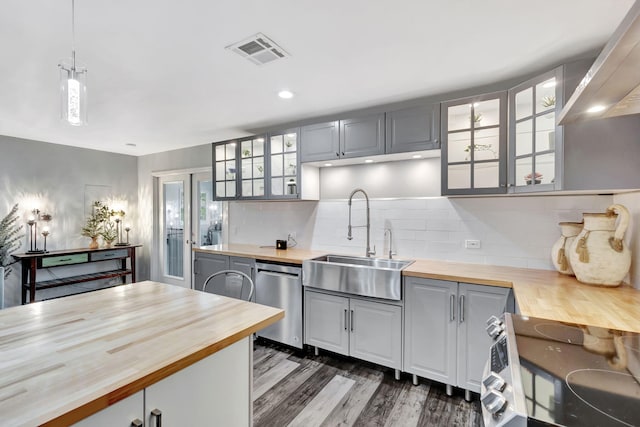 kitchen with visible vents, butcher block counters, glass insert cabinets, stainless steel appliances, and a sink