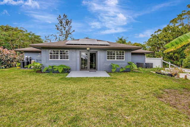 rear view of property with solar panels, a lawn, french doors, a patio area, and stucco siding