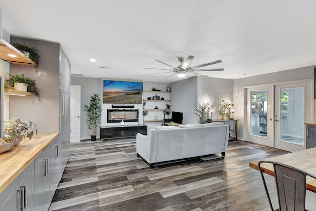 living area featuring recessed lighting, dark wood-type flooring, a ceiling fan, french doors, and a glass covered fireplace