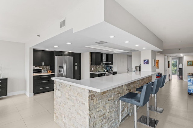 kitchen with tasteful backsplash, a breakfast bar area, appliances with stainless steel finishes, dark cabinets, and wall chimney range hood