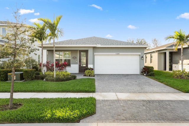 view of front of property with a garage, a shingled roof, decorative driveway, a front lawn, and stucco siding