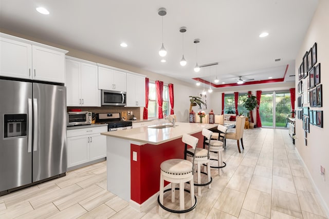 kitchen with a kitchen breakfast bar, hanging light fixtures, a kitchen island with sink, stainless steel appliances, and light countertops