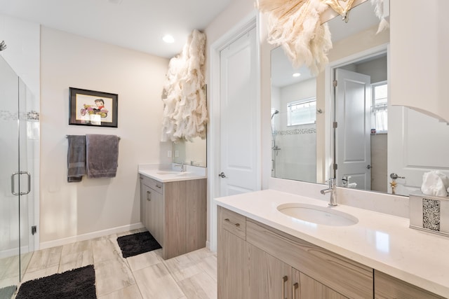 full bath with a stall shower, two vanities, a sink, and baseboards